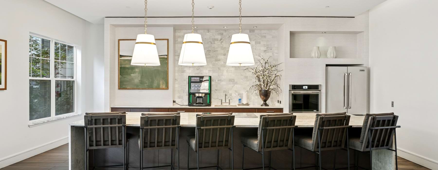 Shared resident lounge at Marq at the Pinehills with island, four bar stools, built-in appliances, light grey flooring, and white walls.