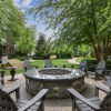 Fire pit at Marq at the Pinehills surrounded by black Adirondack chairs in a landscaped garden with greenery and walking paths.